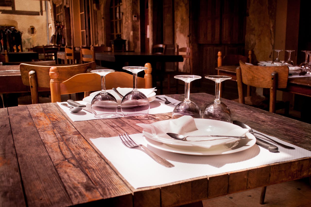 heros-img A rustic restaurant table set with wine glasses and cutlery invites guests to dine.